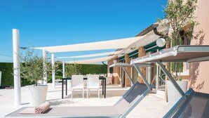 A sunlit outdoor seating area with lounge chairs and a table, surrounded by a white canopy and a green hedge. - VIOLET Luxury Apt in Villa, Patio, Pool, Hot Jacuzzi, A/C, WiFi, Gym, Sauna (San Pietro di Cavarzere VE)