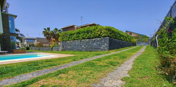 A modern residential area with a swimming pool, stone retaining wall, and a stone pathway. - Villa Gloria Maria, Swimming Pool - CIN:IT087024C2QQKFD6UP (Mascalucia)