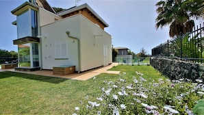 A modern two-story house with a large glass window, a stone wall, and a well-maintained lawn with flowers. - Villa Gloria Maria, Swimming Pool - CIN:IT087024C2QQKFD6UP (Mascalucia)