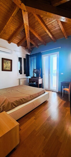 Une chambre avec un plafond en bois, un lit, un bureau, une chaise et une fenêtre avec des rideaux.