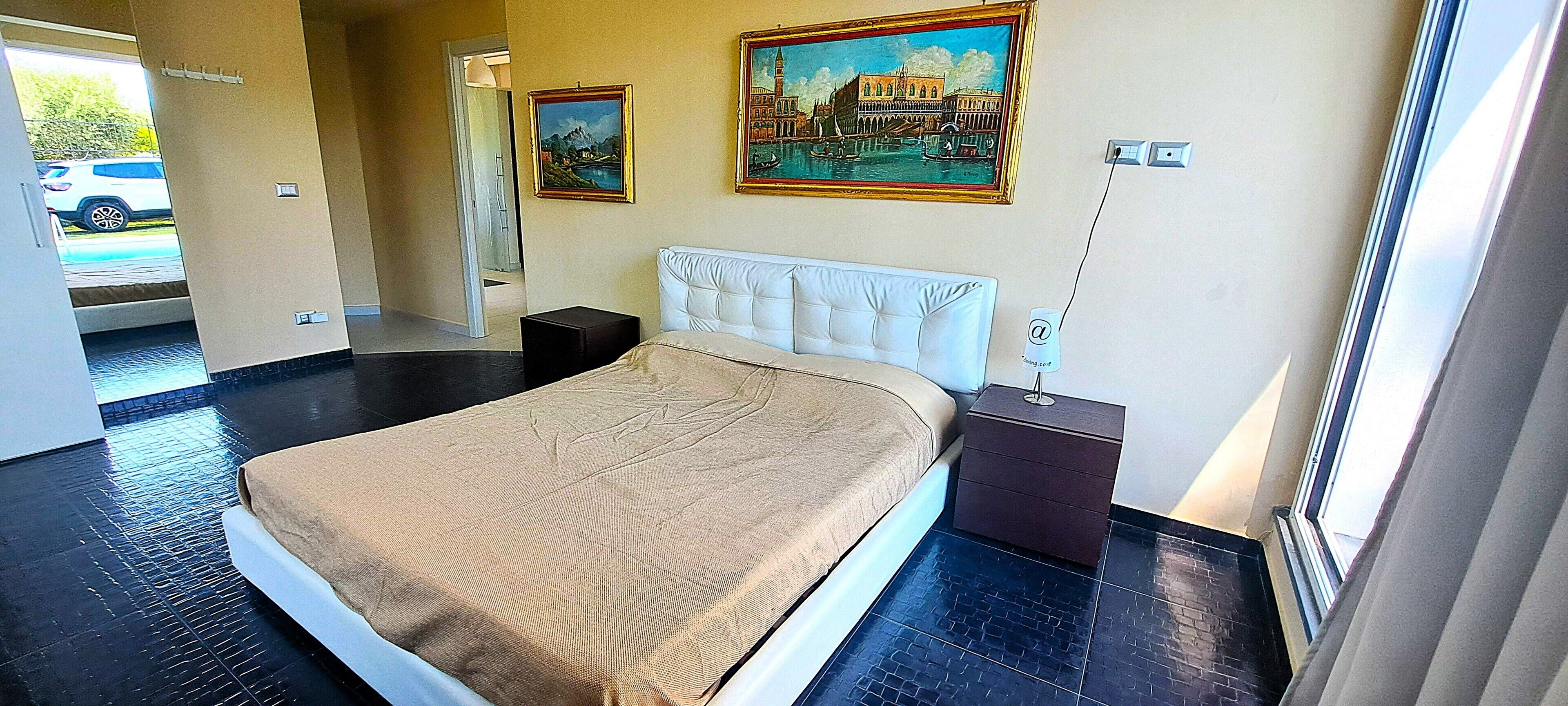 Una habitación de hotel con cama, mesitas de noche, un cuadro y una ventana.