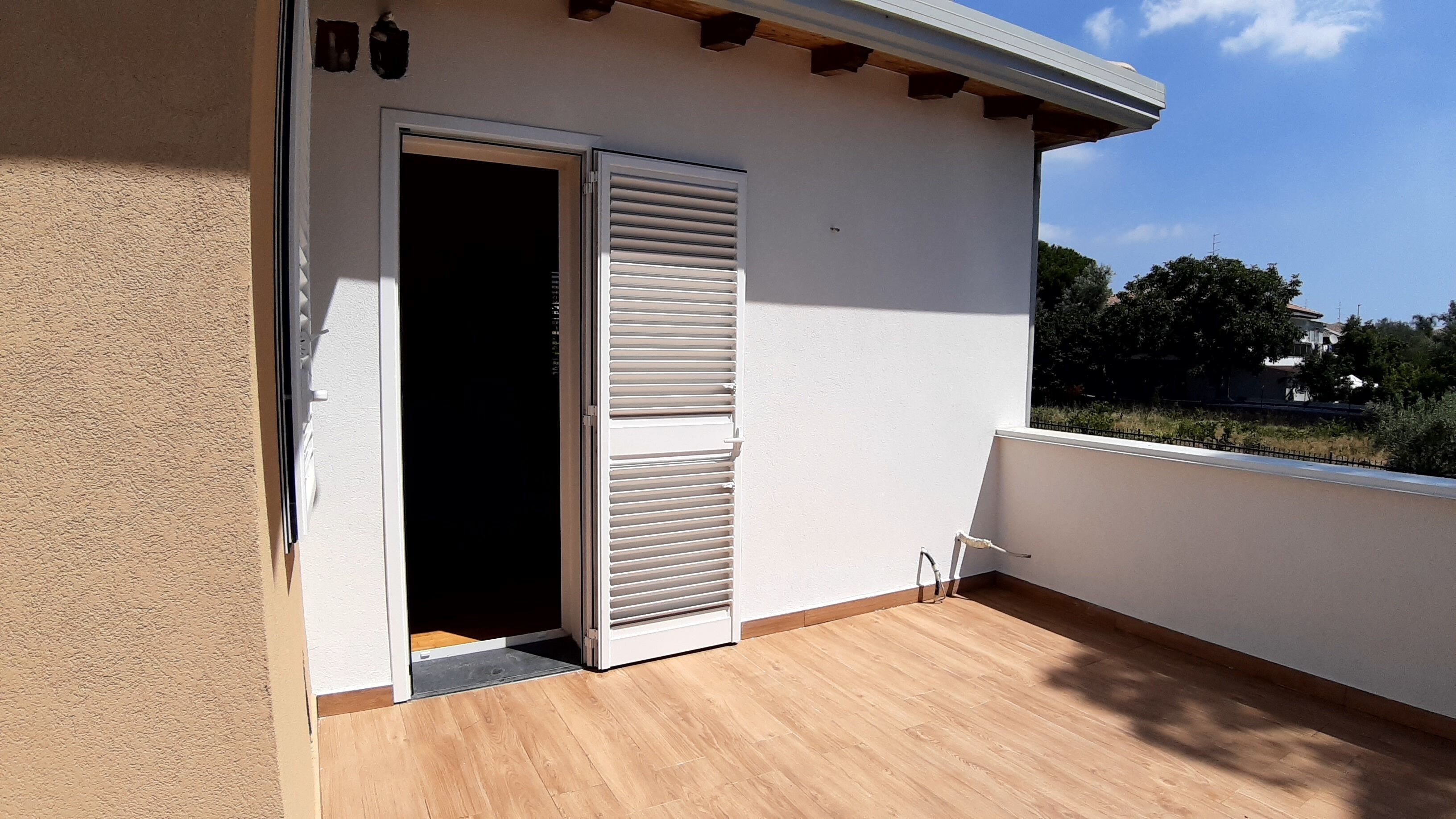 Un balcon doté d’un plancher en bois, d’un mur blanc et d’une porte avec des volets.
