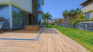 A modern outdoor patio with wooden flooring, a stone wall, and a glass enclosure. - Villa Gloria Maria, Swimming Pool - CIN:IT087024C2QQKFD6UP (Mascalucia)