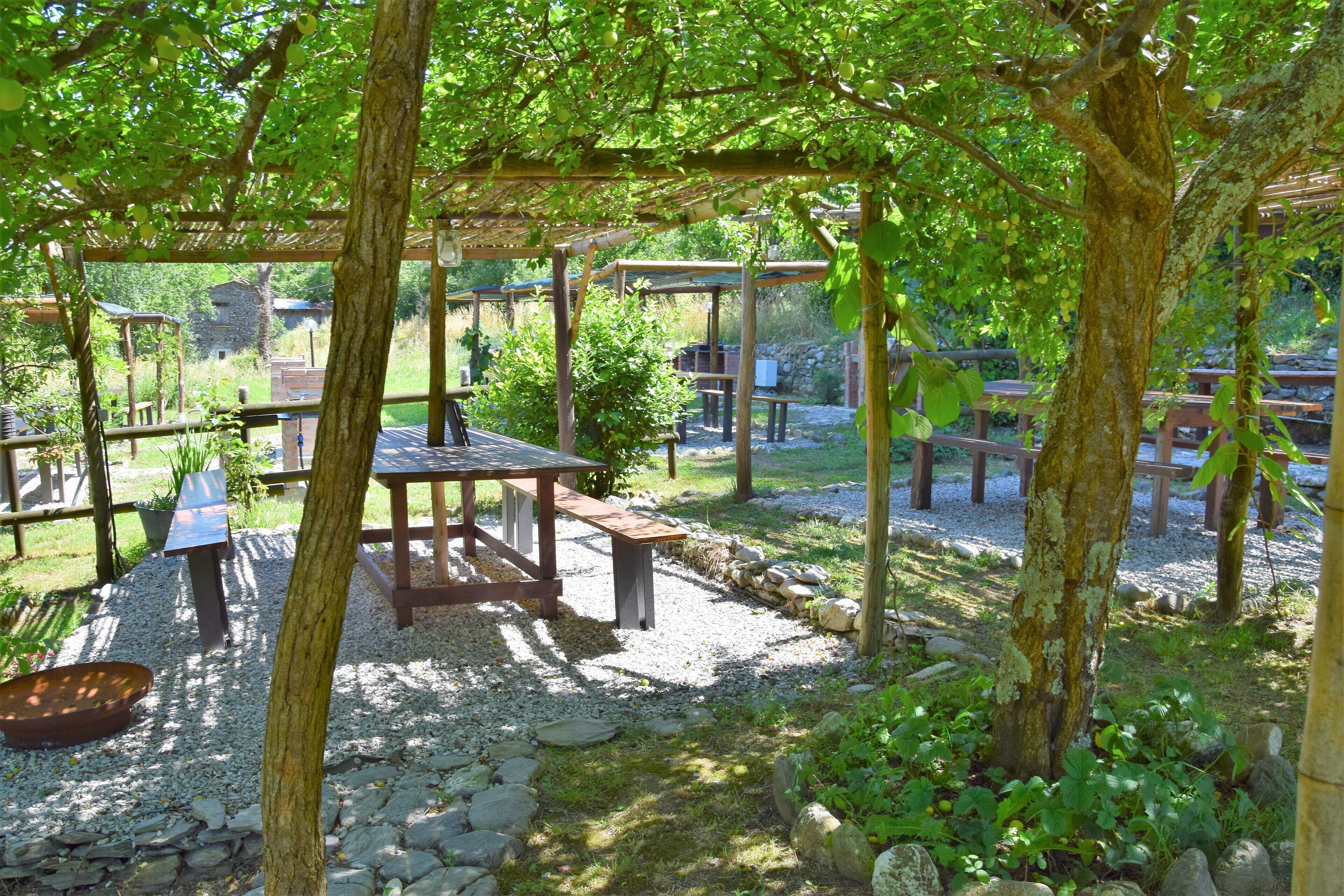 Ulkona sijaitseva puutarha, jossa on puisia pergola-rakenteita, pöytiä ja penkkejä.