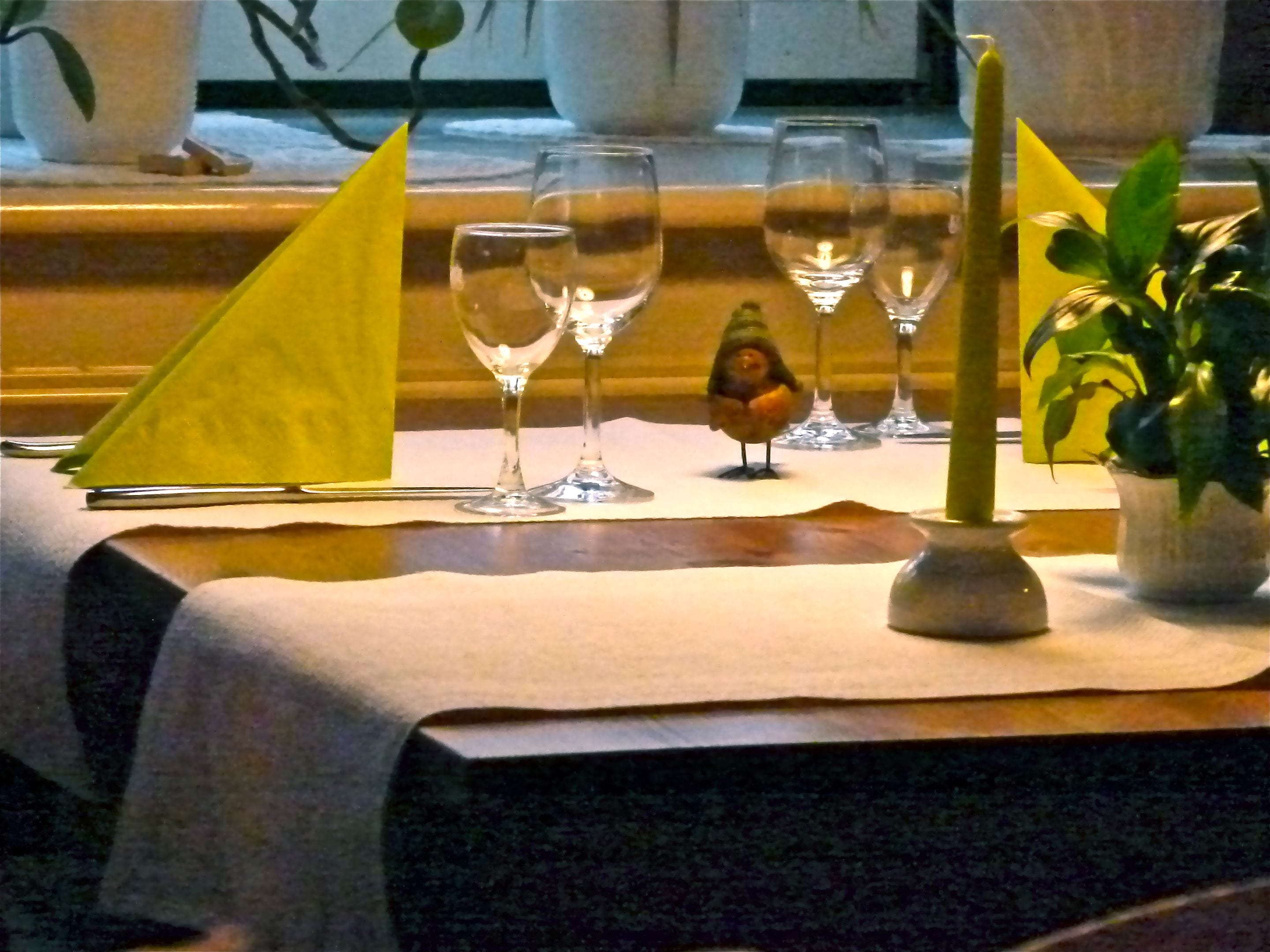 Una mesa servida con copas de vino, una figurita de pájaro y una vela.