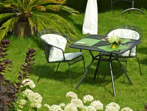 Un espacio al aire libre con una mesa y dos sillas, rodeado de césped y plantas.