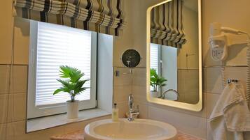 Une salle de bain avec un grand miroir, un lavabo, un porte-serviettes et une plante en pot.