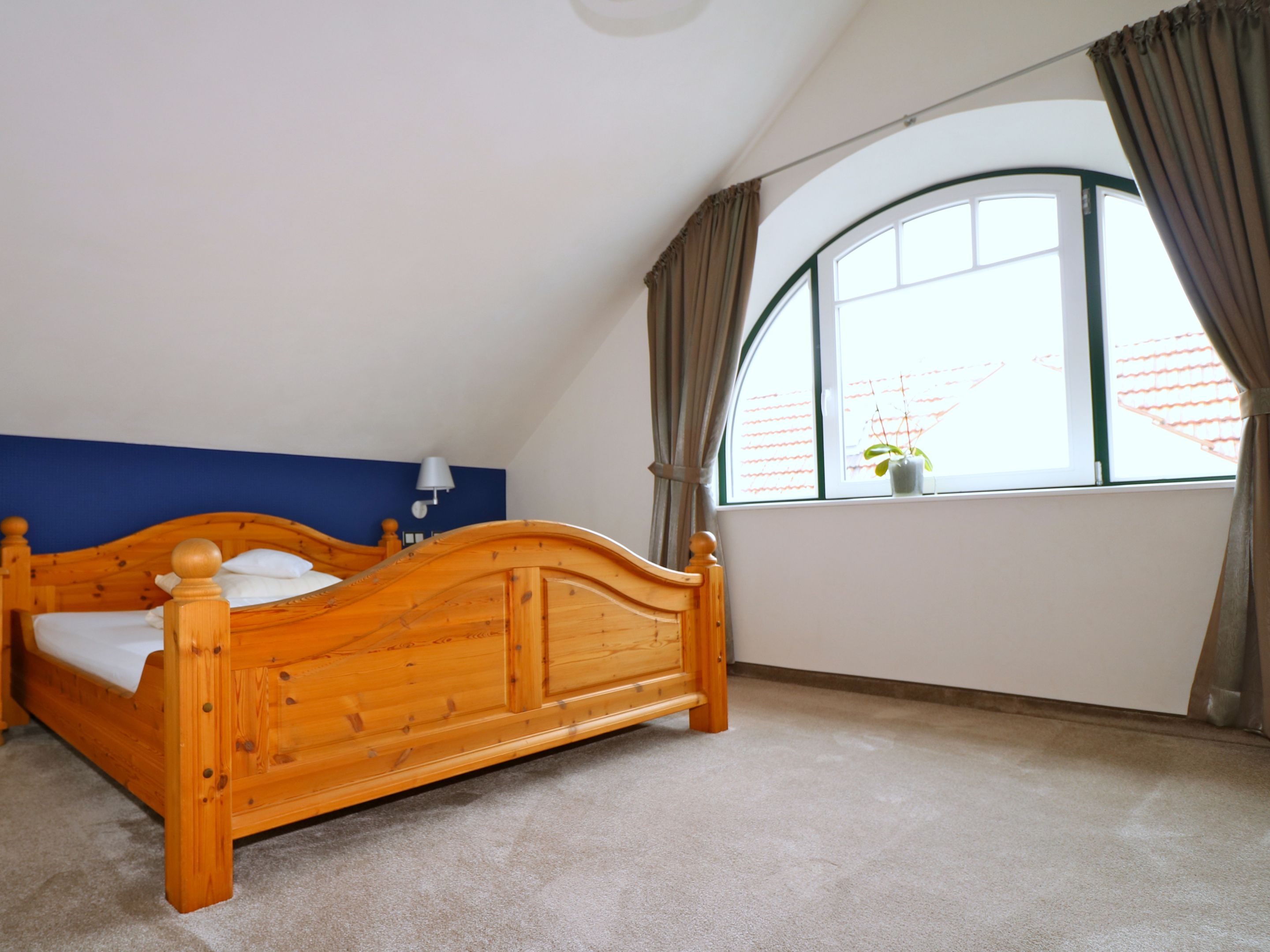 A bedroom with a wooden bed, a blue accent wall, a window with curtains, and a small plant on the windowsill.