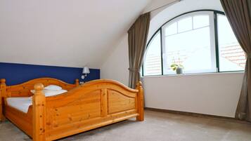 A bedroom with a wooden bed, a blue accent wall, a window with curtains, and a small plant on the windowsill.