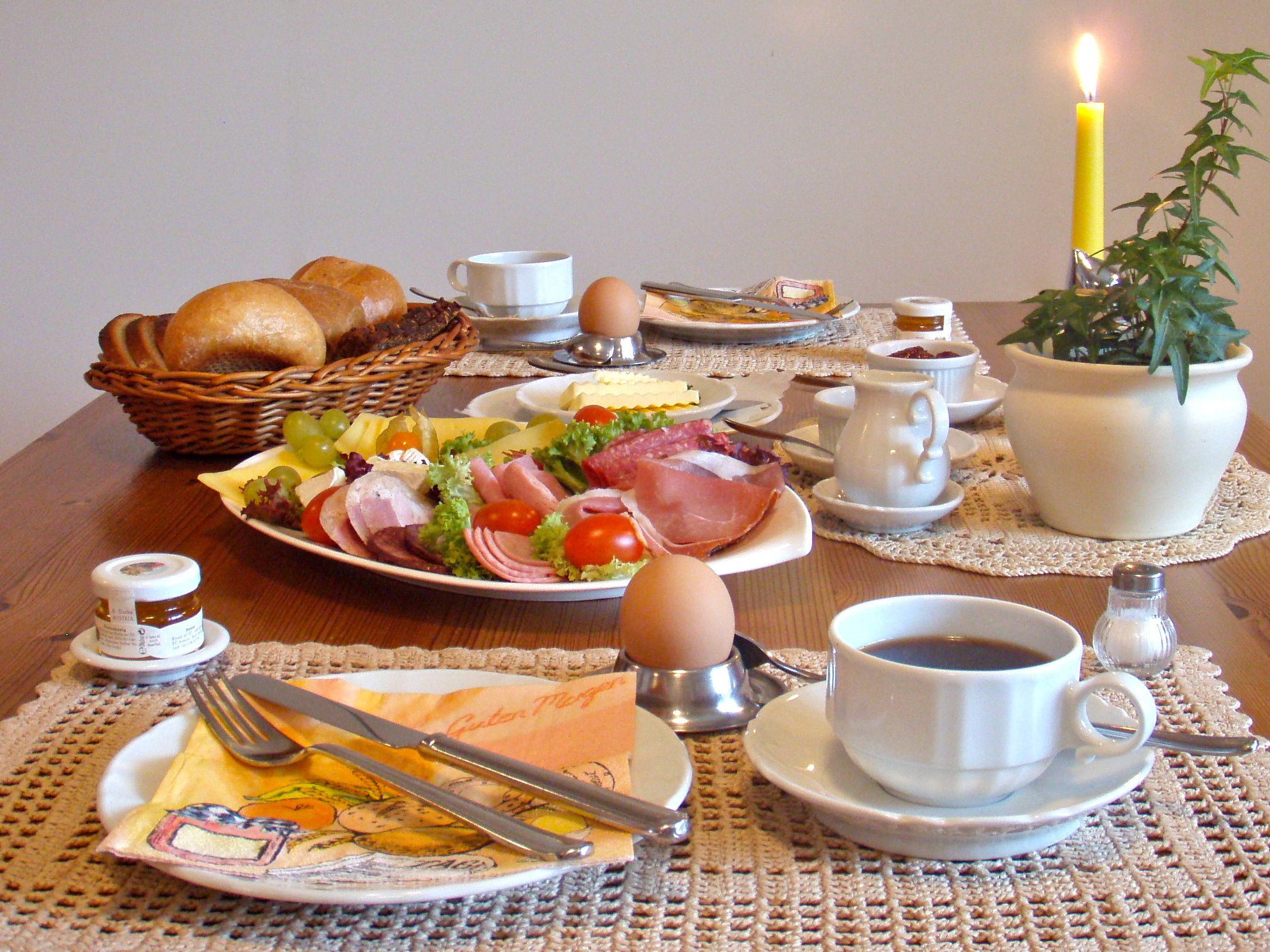 Una mesa de desayuno con pan, huevos, jamón, queso y una taza de café.