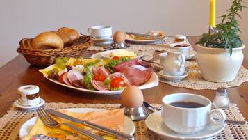 Una mesa de desayuno con pan, huevos, jamón, queso y una taza de café.