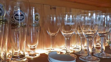 A row of empty wine glasses and a bottle of Schneider Weisse beer on a wooden shelf.