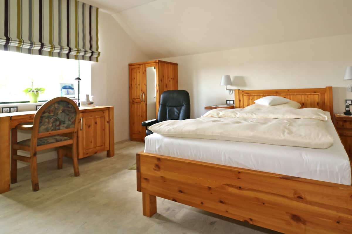 Un dormitorio con cama de madera, un escritorio, una silla, un armario y una ventana con cortinas.