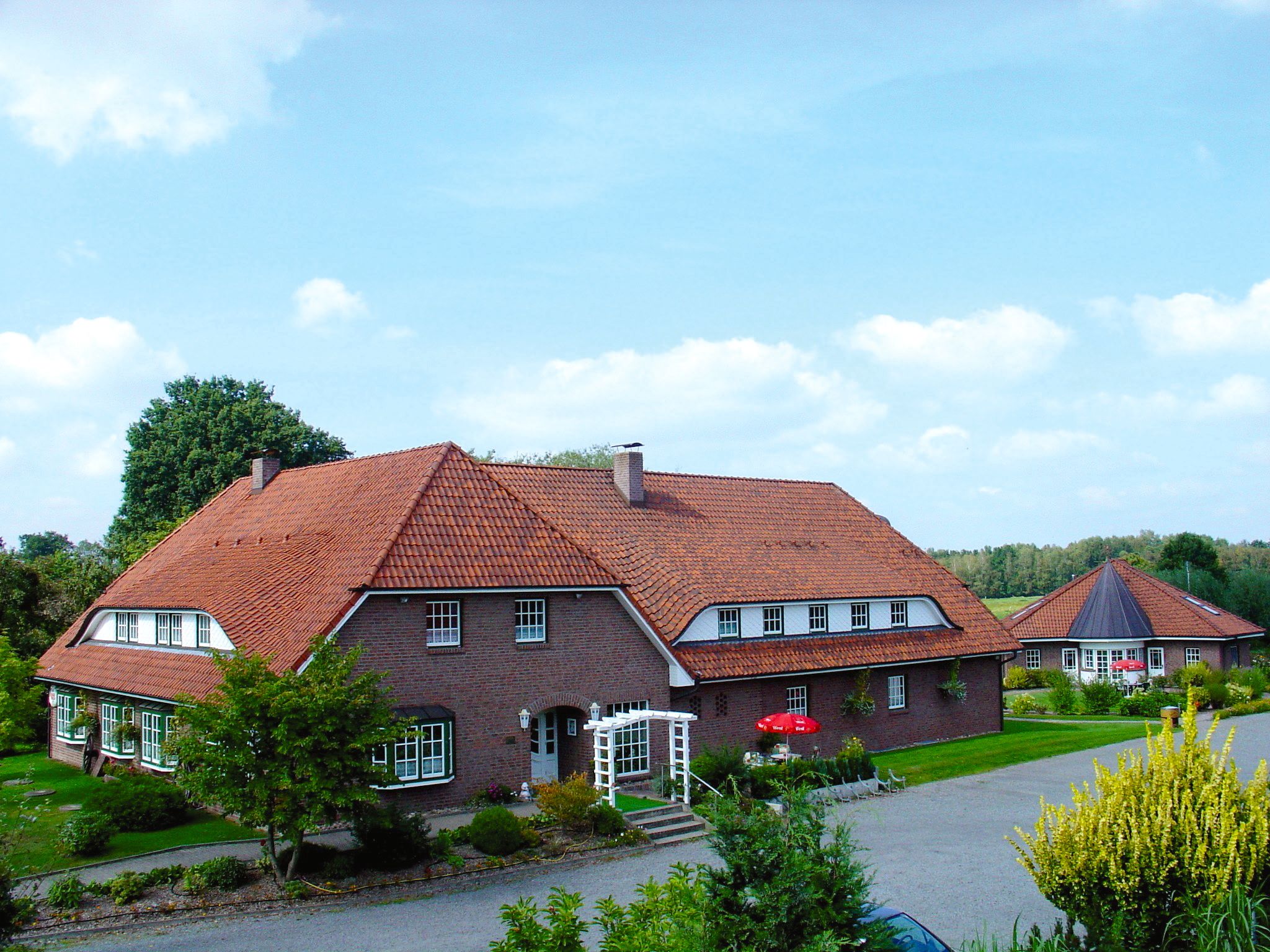 Ett stort hus byggt av tegel med ett rött tegeltak, en veranda och en välskött trädgård.