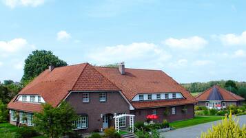 Ett stort hus byggt av tegel med ett rött tegeltak, en veranda och en välskött trädgård.