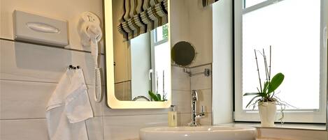 A modern bathroom with a large mirror, a sink, a hairdryer, and a potted plant by the window.