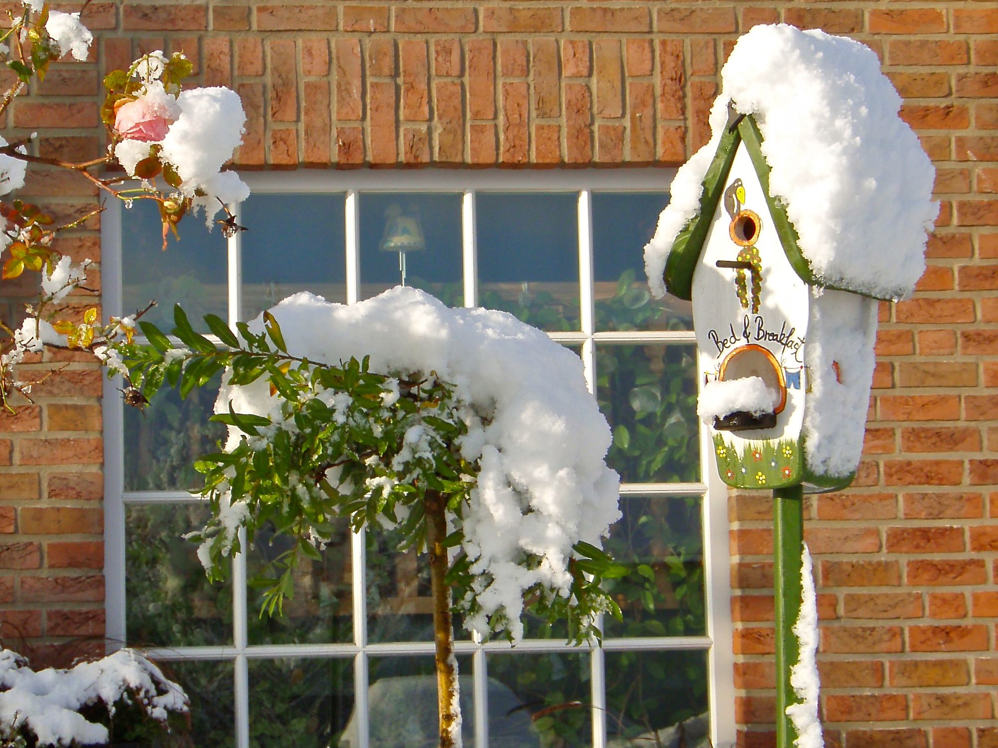 Un edificio in mattoni con una finestra e una casetta per uccelli, il tutto imbiancato dalla neve.