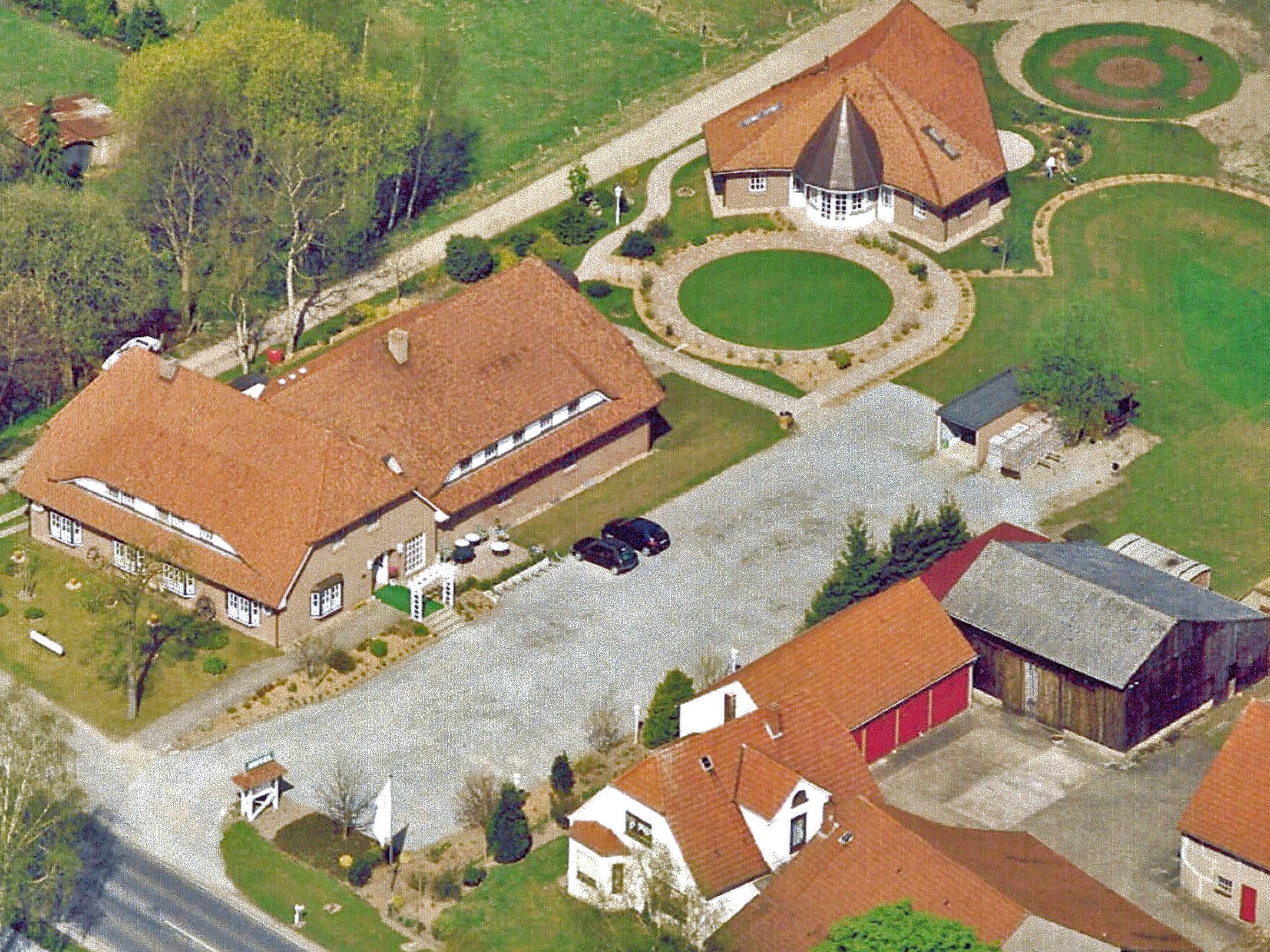 An aerial view of a residential area with a large house featuring a central courtyard, a smaller attached building, and a barn.