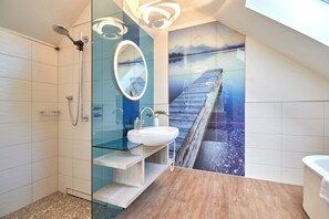 Un baño moderno con cabina de ducha de vidrio, un lavamanos blanco y un espejo grande.