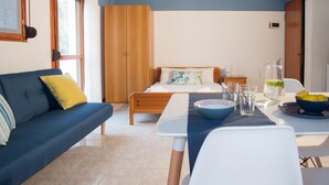 Una stanza con un letto, un divano, un tavolo con una ciotola e dei bicchieri, e una caraffa d'acqua.