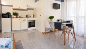 Una cucina moderna con mobili bianchi, un forno a microonde, un tostapane e un forno. È presente un tavolo da pranzo con sedie e una pianta in vaso.