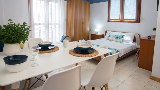 Una stanza con un letto, un tavolo da pranzo con sedie, una pianta in vaso e una finestra con tende.