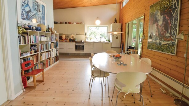 Une cuisine moderne avec des meubles blancs, un îlot central et un coin repas comprenant une table ronde et des chaises blanches.