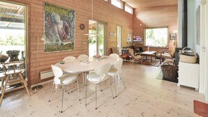 Une pièce spacieuse avec un grand plafond en bois, une table à manger ronde entourée de chaises blanches et une grande affiche accrochée au mur.