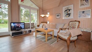 Ein gemütliches Wohnzimmer mit Holzboden, Fernseher, Sofa und Sessel.