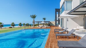 Un área de piscina moderna con cubierta de madera, sillas de descanso y vistas al océano.