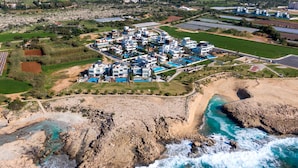 Vista aérea de un complejo turístico costero con edificios modernos, una playa y un litoral rocoso.