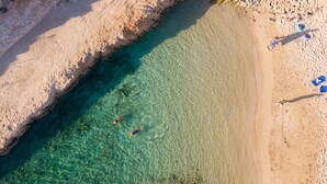 Vista aérea de una playa con agua turquesa cristalina, una orilla arenosa y algunas personas nadando.