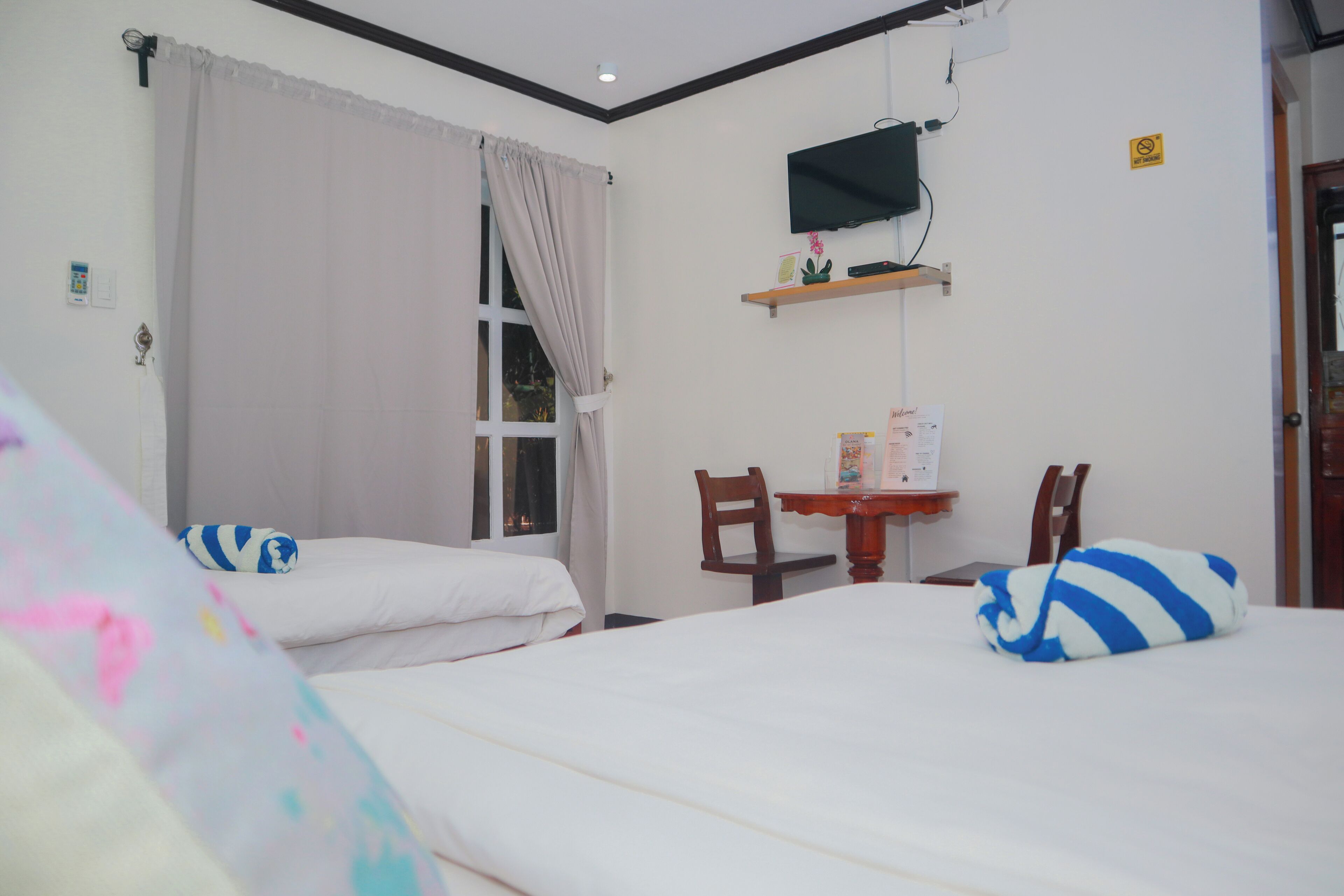 Habitación de hotel con dos camas, un escritorio, una silla, un televisor y una ventana con cortinas.