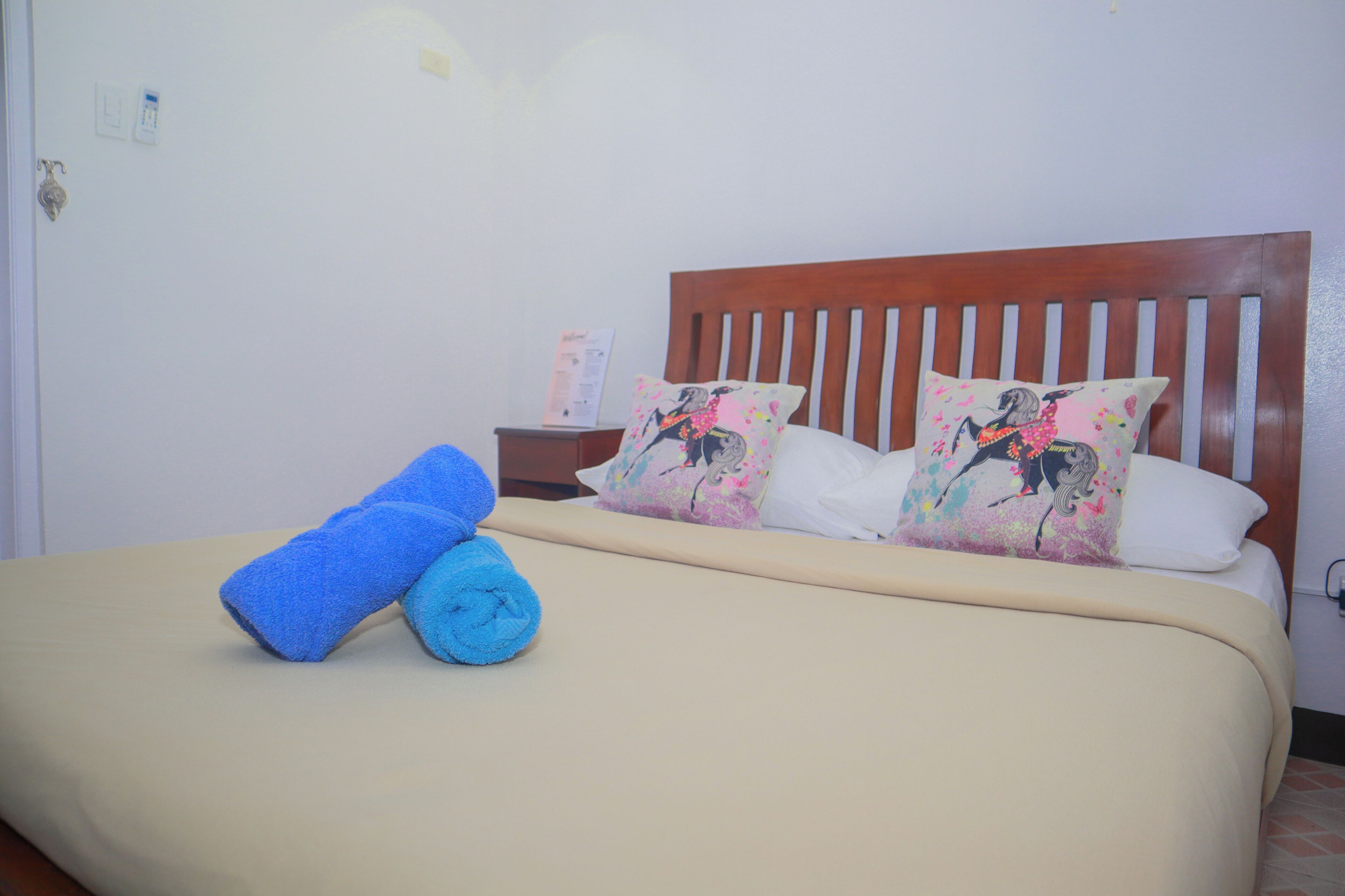 A bed with a wooden headboard, two pillows with floral designs, and two rolled towels on the bed.
