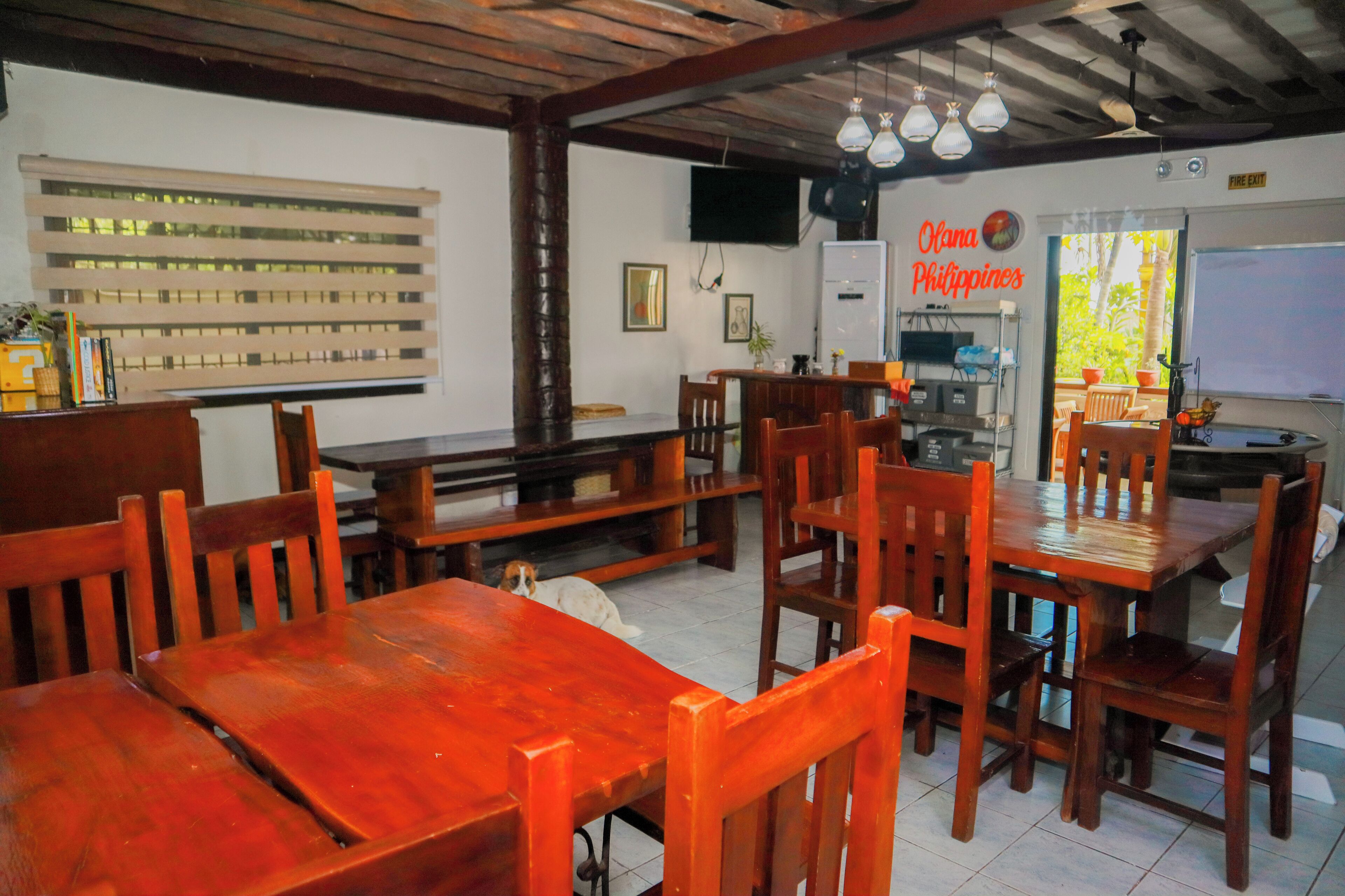 A dining area with wooden tables and chairs, a television mounted on the wall, and a sign reading "Olana Philippines".