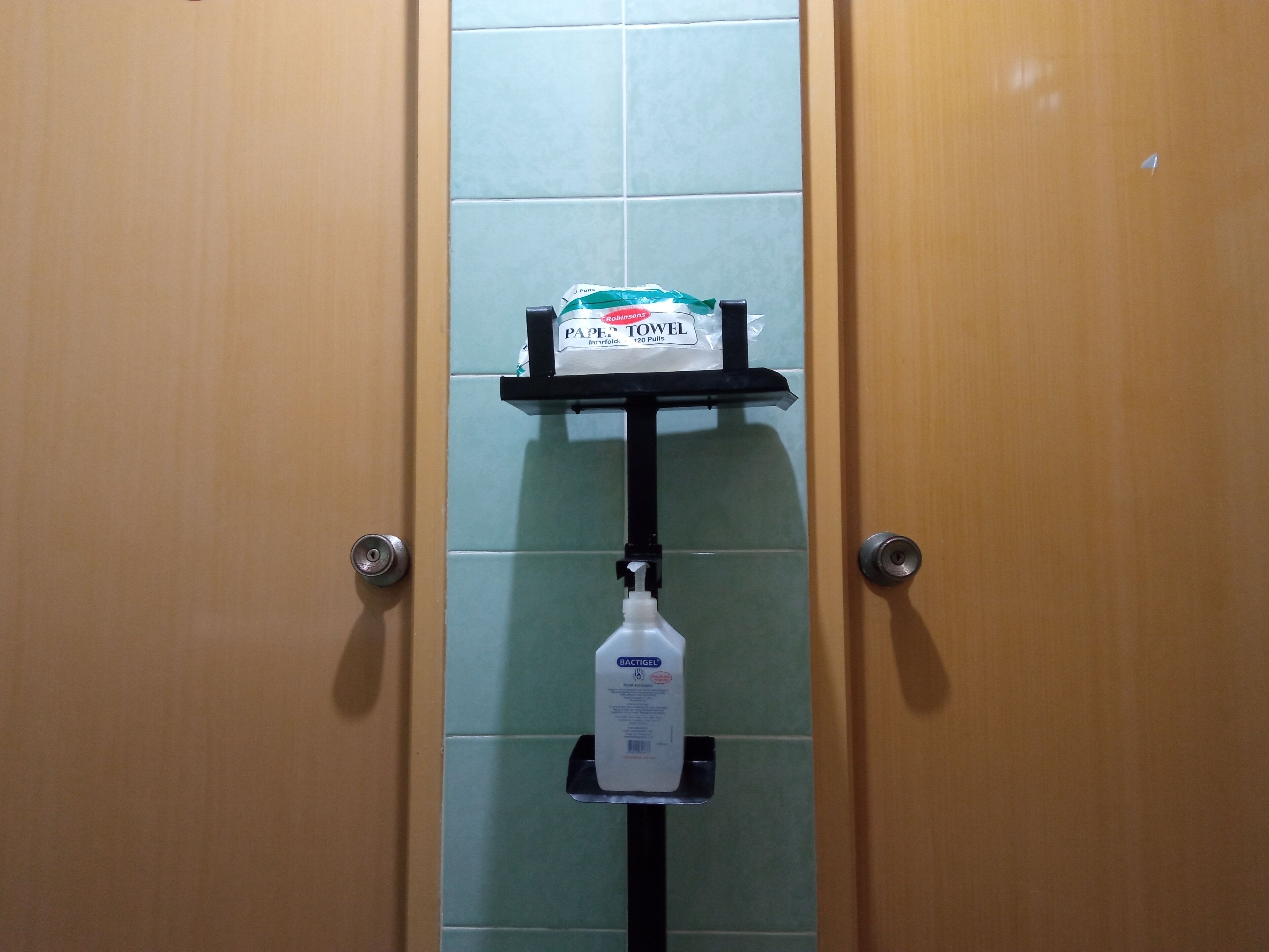 Une salle de bain équipée d’un distributeur d’essuie-tout et d’un flacon de gel hydroalcoolique, le tout placé sur une étagère fixée au mur.
