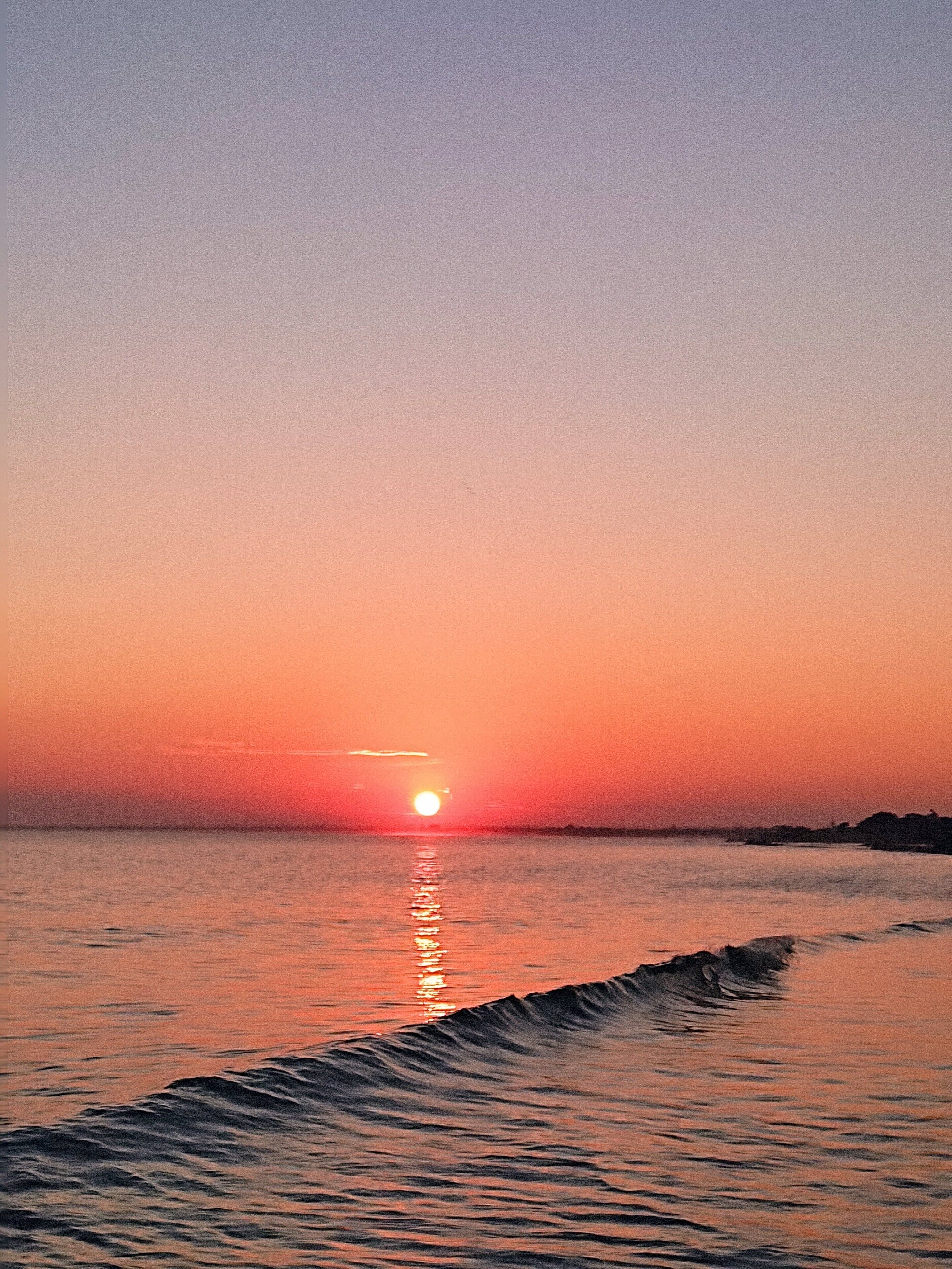 Ein Sonnenuntergang über einem ruhigen Meer mit sanften Wellen.