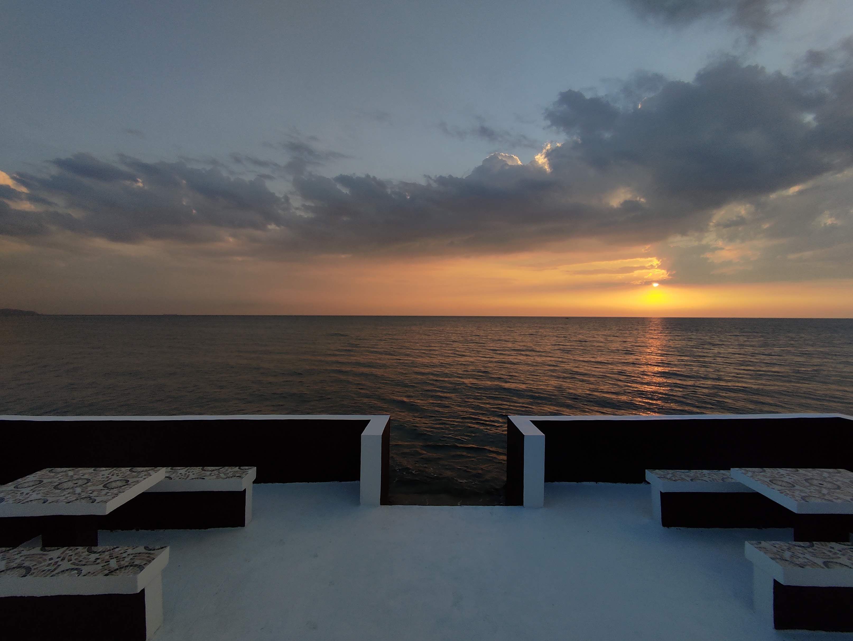 Vista al atardecer desde una terraza con dos zonas de estar mirando al mar.