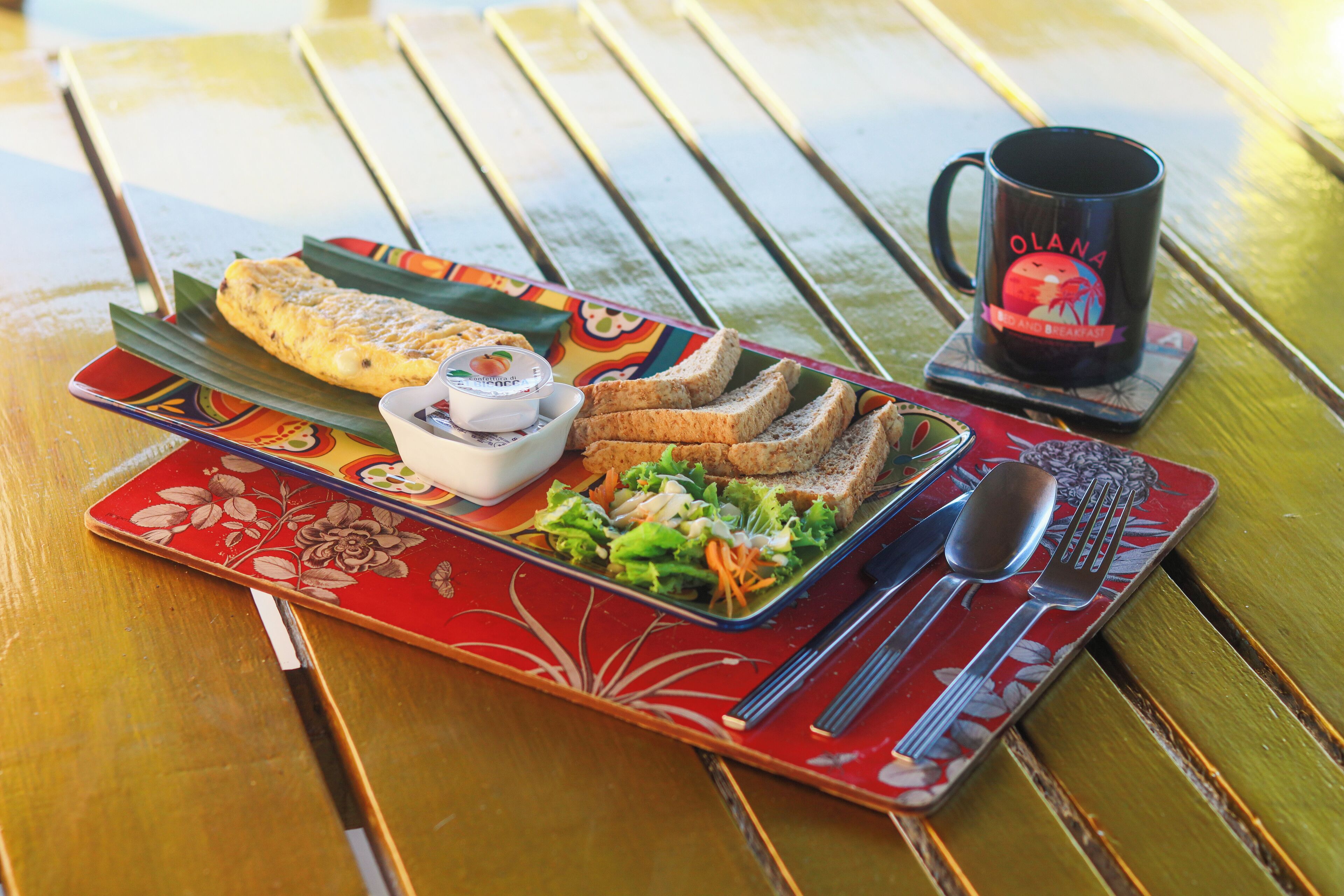 A meal on a wooden table with a red and white plate, a black mug, and a spoon and fork.