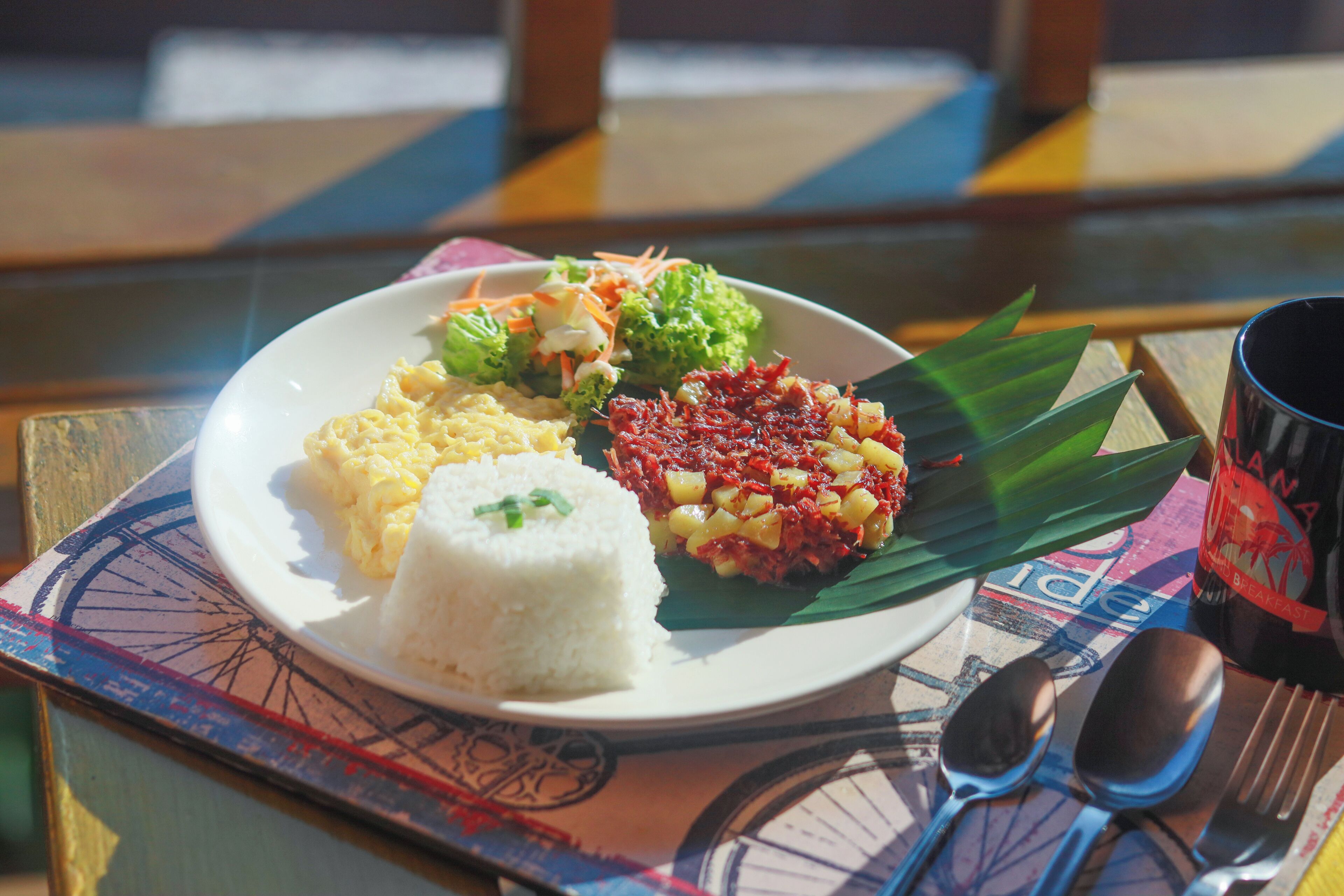Un plato con arroz, huevos revueltos y un guiso de verduras sobre una mesa con un mantel individual con motivos de bicicleta.