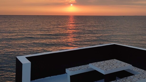 A sunset over the ocean with a view of the sea and a seating area with patterned cushions.