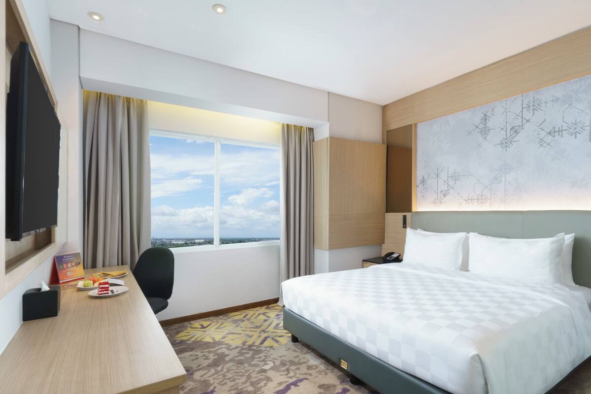 Habitación de hotel con una cama grande, un escritorio con silla, un televisor de pantalla plana y una ventana con cortinas.