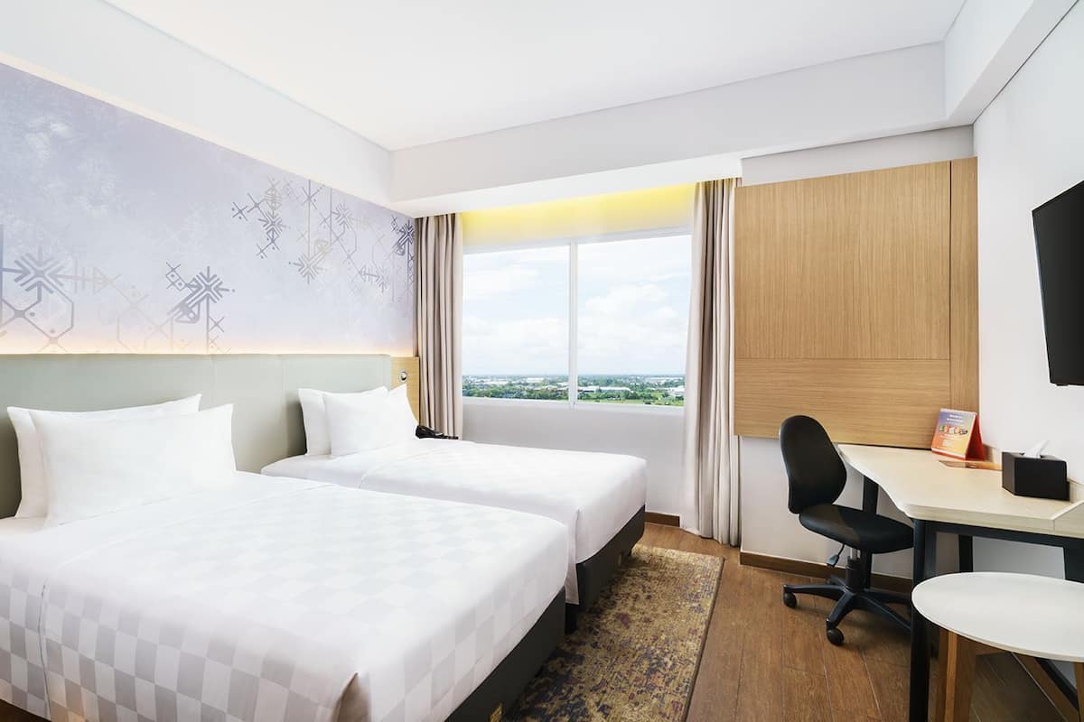 Habitación de hotel con dos camas, un escritorio, una silla, un televisor y una ventana con vistas.