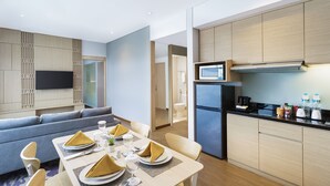 Habitación de hotel moderna con zona de comedor, sofá, televisor de pantalla plana, cocina equipada con refrigerador y microondas.