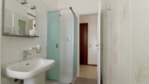 Ein Badezimmer mit einem weißen Waschbecken, einer Duschkabine aus Glas und einem Spiegel über dem Waschbecken.