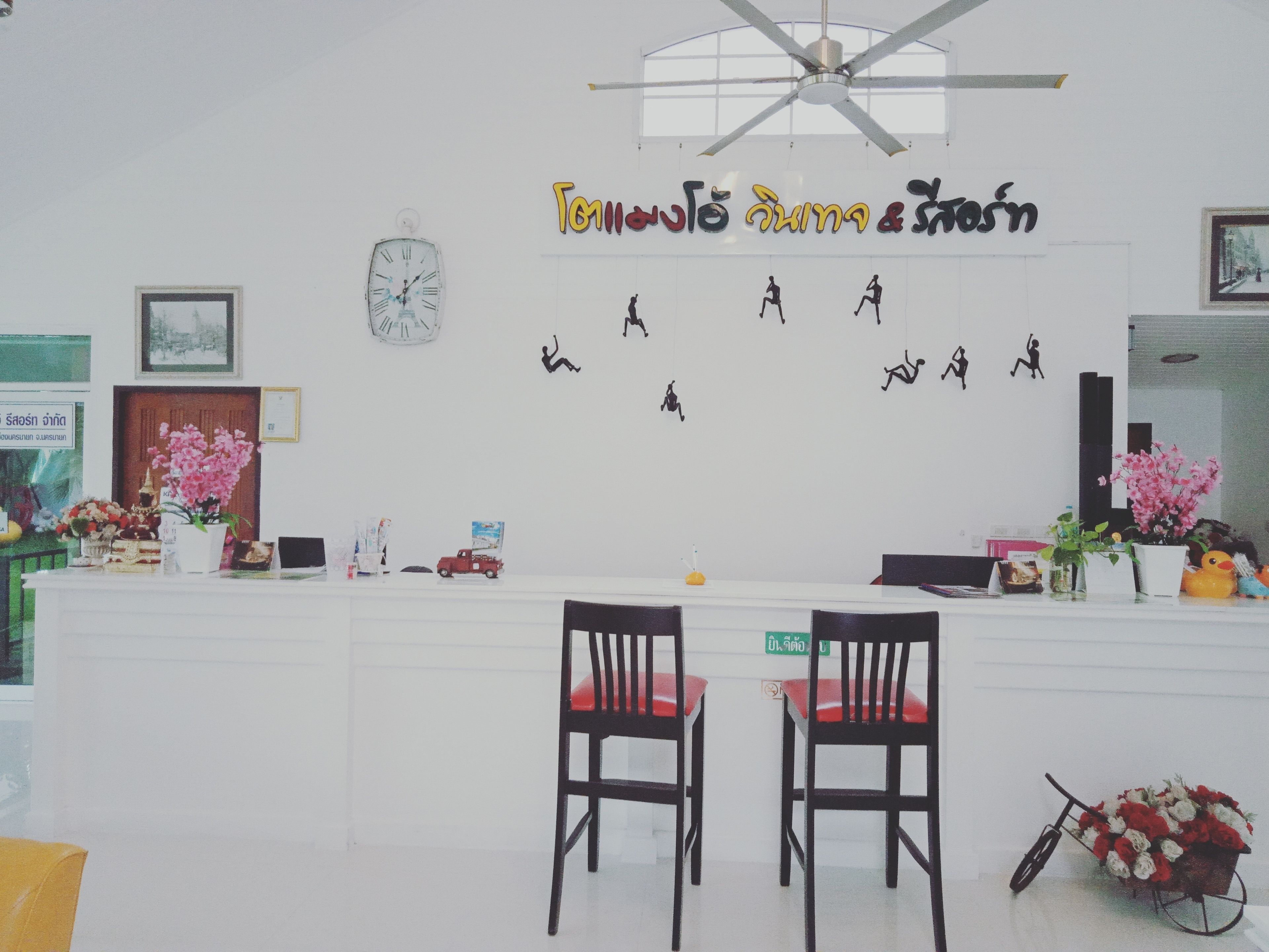 Un mostrador de recepción con dos sillas, un reloj y adornos de pared que incluyen un letrero y siluetas de personas.
