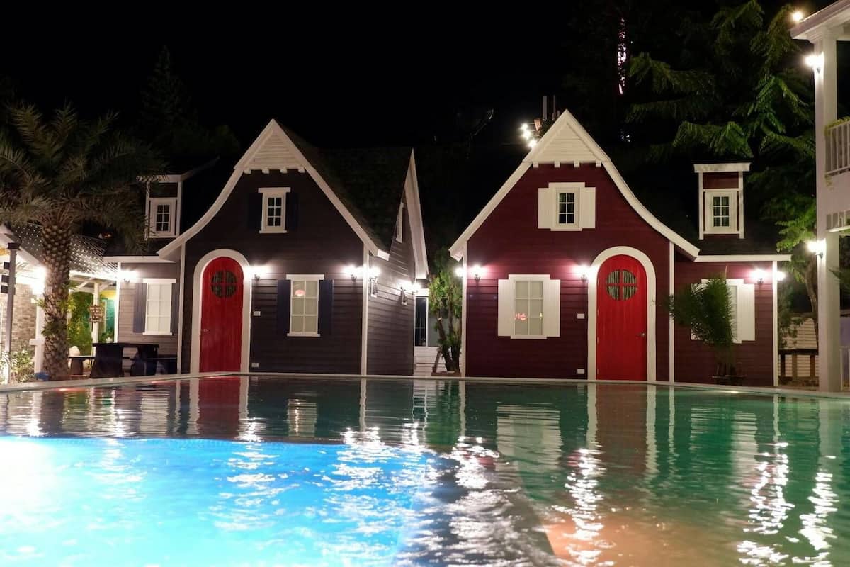 A swimming pool area with two red-roofed buildings, each with a window and a door, and a small structure with a white door.