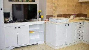 Une cuisine avec des meubles blancs, un téléviseur à écran plat, une machine à café et un grille-pain.