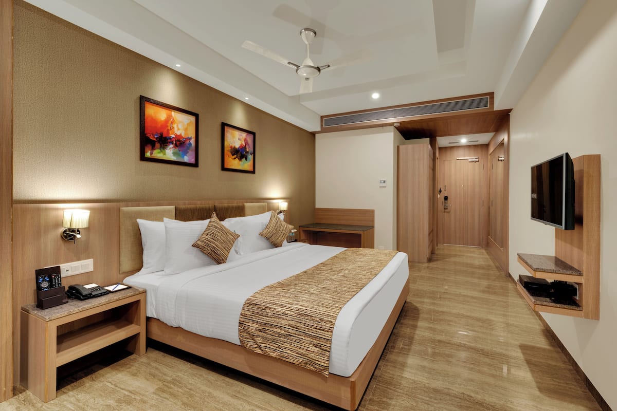 A hotel room with a bed, bedside tables, a TV, and artwork on the wall.