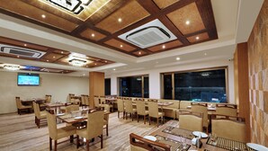 Un vaste espace dédié à la salle à manger, avec de nombreuses tables et chaises, de grandes fenêtres et un écran de télévision fixé au mur.